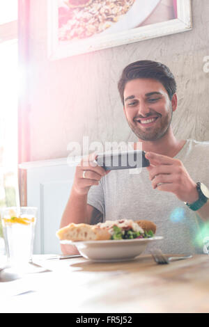 Smiling man photographing lunch at cafe table Stock Photo