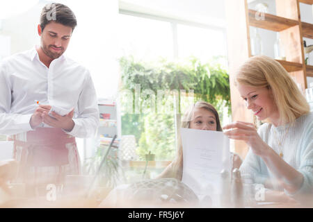 Waiter taking order from mother and daughter in cafe Stock Photo