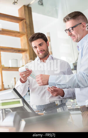 Cafe owner and waiter reviewing receipt at cash register Stock Photo