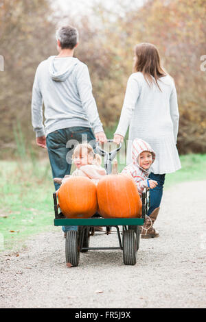 Parents pulling toddler children and pumpkins riding in wagon Stock Photo