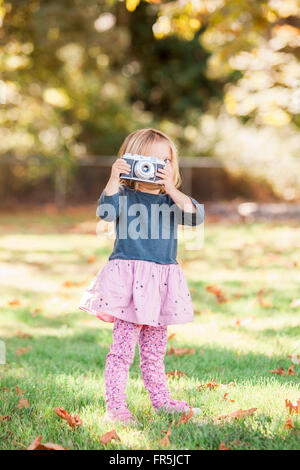 Toddler girl using retro camera in autumn park Stock Photo