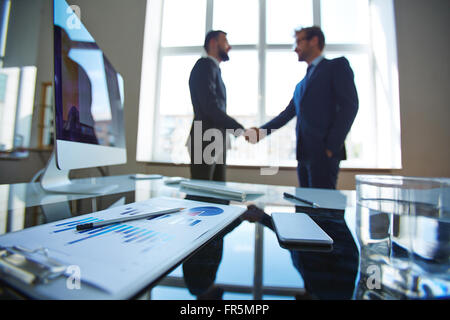 Close-up of workplace with documents with businessmen in the background Stock Photo