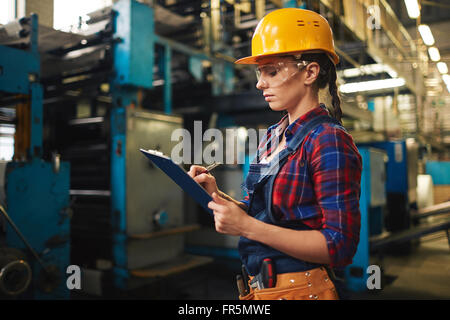 Young woman making notes in document in factory Stock Photo
