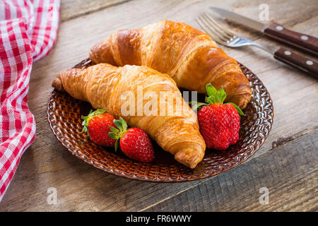 Fresh croissants with strawberries on plate on wooden background. Continental breakfast food, warm tone Stock Photo