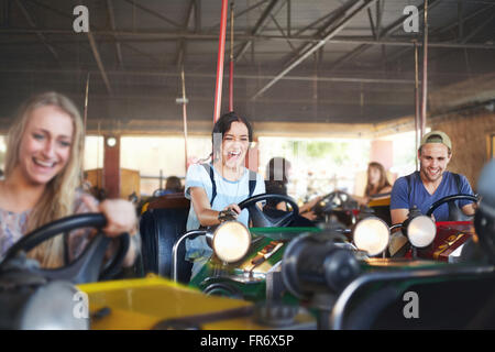 Enthusiastic friends riding bumper cars at amusement park Stock Photo