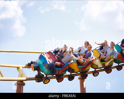 Friends cheering and riding roller coaster at amusement park Stock Photo