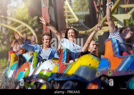 Enthusiastic friends cheering on roller coaster at amusement park Stock Photo
