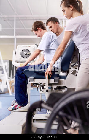 Physical therapists guiding man using equipment Stock Photo