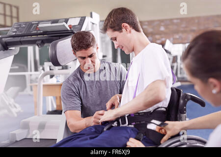 Physical therapists attaching equipment to man in wheelchair Stock Photo