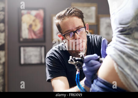 Tattoo artist tattooing woman’s back Stock Photo