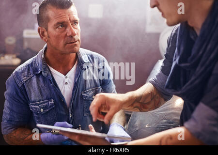 Man with digital tablet talking to tattoo artist Stock Photo