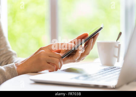 Woman at home consult her mobile phone near laptop. Blur Garden background Stock Photo