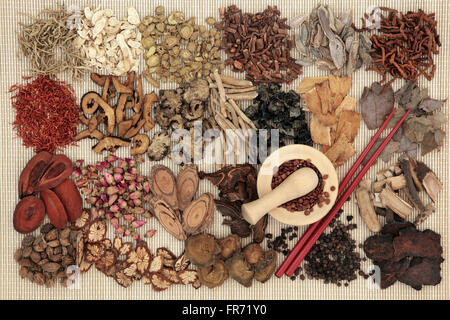 Traditional chinese herbal medicine ingredients over bamboo background with mortar and pestle and chopsticks. Stock Photo