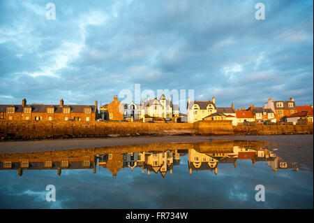 20/03/2016, The sun sets on a row of houses reflected in the water at Elie, a coastal town in the East Neuk of Fife, Scotland. Stock Photo