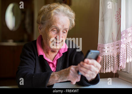 Elderly woman sitting at table typing on a smartphone. Stock Photo
