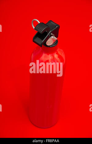 A small fire extinguisher standing on a red surface ready to be used. The lock pin and sealing is intact. Stock Photo