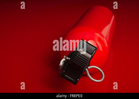 A small fire extinguisher lying on a red surface with the top nozzle pointing out of the image Stock Photo