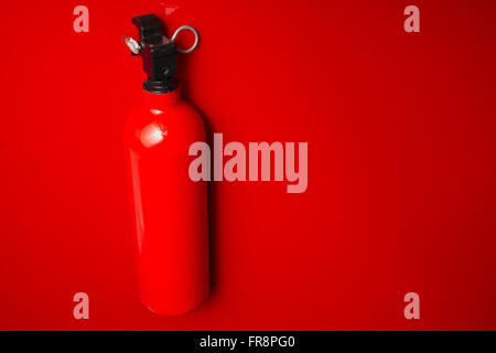 A small fire extinguisher hanging on a red wall ready to use. The lock pin and sealing is intact. Stock Photo