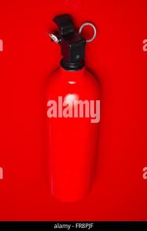 A small fire extinguisher hanging on a red wall ready to use. The lock pin and sealing is intact. Stock Photo