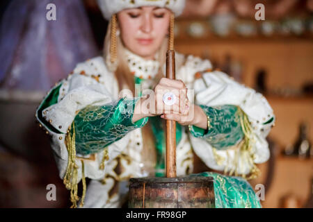 Young woman in traditional dress producing butter from milk at home. Stock Photo