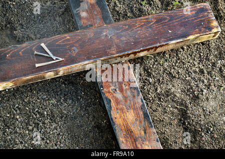 Wooden Cross laying on the ground with three nails nearby Stock Photo