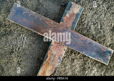 Wooden Cross laying on the ground with three nails nearby Stock Photo