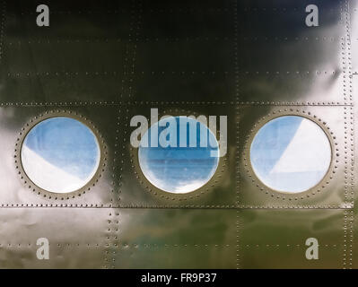 Portholes on military green painted metal background with rivet. Three portholes on board old retro airplane. Stock Photo