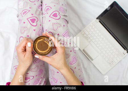 Woman having a cup of coffee in bed with a notebook Stock Photo