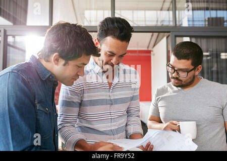 Creative team working on their business project together at office. Three young men looking at some documents in a small meeting Stock Photo