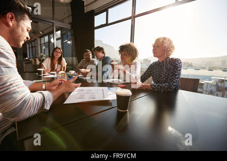 Portrait of creative team sitting around a table discussing new project plans. Mixed race people meeting in office. Stock Photo