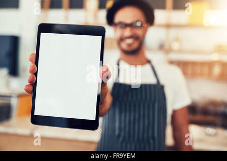 Close up portrait of a waiter holding up a tablet computer with a empty display. Coffee shop owner showing a digital tablet. Stock Photo