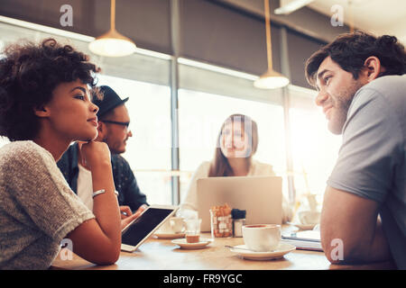 Portrait of group of young people sitting at a cafe and discussing work. Young men and women at coffee shop for startup meeting. Stock Photo