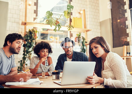 Portrait of young creative team sitting at a cafe and looking at a laptop. Young woman giving business presentation on laptop to Stock Photo