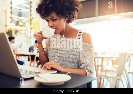 Portrait of young african woman drinking coffee and using laptop at a cafe. Stock Photo