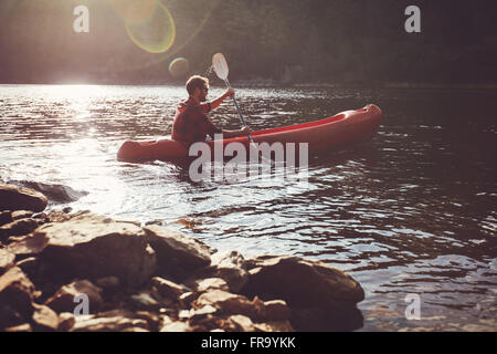 Young man kayaking in a lake. Young guy paddles his kayak on a sunny day.