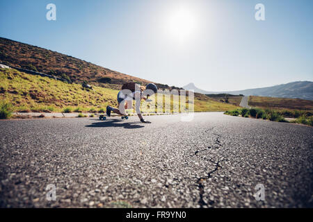 Rear view of young female skater practicing skateboarding on rural roads on a sunny day. She is doing stunts and touching the ro Stock Photo