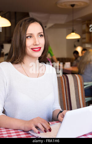 Young happy woman using notebook in cafe. Pretty girl working with laptop in the restaurant. Stock Photo