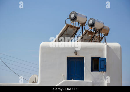 Modern solar panel powered hot water heaters for energy efficiency are mounted on the roof of a traditional greek home; Mykonos, Greece Stock Photo