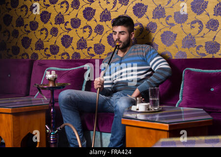 Young Man Smoking Shisha At Arabic Restaurant - Man Exhaling Smoke Inhaling From A Hookah Stock Photo