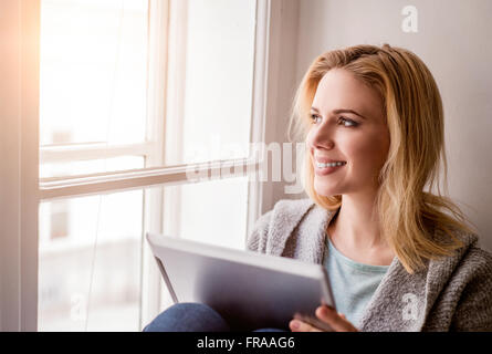Woman with tablet sitting on window sill, sunny day