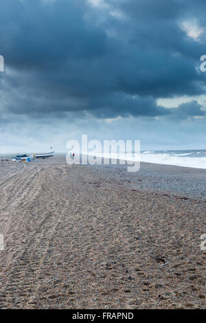 Distant people and boats on stormy beach in winter, Cley North Norfolk UK Stock Photo