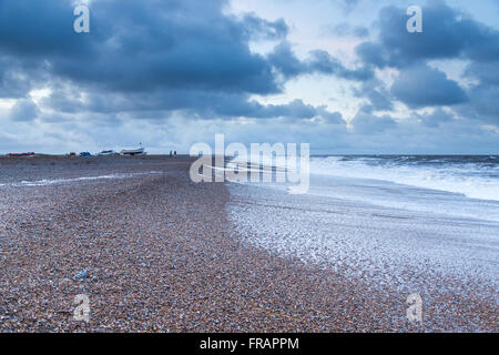 Distant people and boats on stormy beach in winter, Cley North Norfolk UK Stock Photo