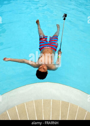 Colorful, graphic image of 12 year old boy lying on his back in a swimming pool, holding a go pro camera on a camera stick . Stock Photo