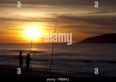 People fishing on the beach of Santa Catarina coast at sunrise and island in the background Stock Photo