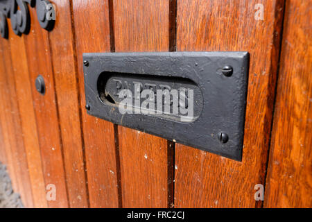 Slot in a wood door with papers written on it to be used as a mailbox at an urban historic building. Stock Photo