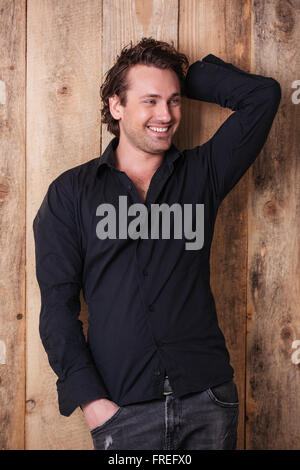 Smiling attractive young man in black shirt standing and posing over wooden background Stock Photo