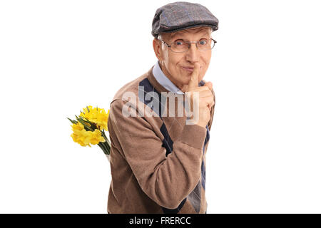 Romantic senior holding a bunch of flowers behind his back and gesturing silence isolated on white background Stock Photo