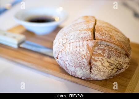 A freshly baked loaf of crusty bread and dipping olive oil and balsamic vinegar on a cutting board. Stock Photo