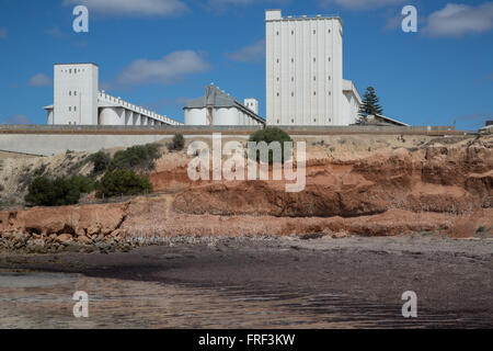 white crop storage silo facilities on top of sea shore brim with muddy sand in front Stock Photo