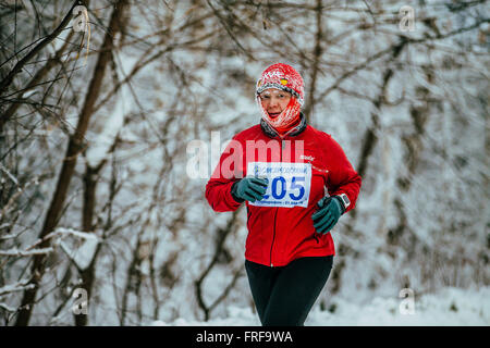 middle-aged woman athlete running on winter snow-covered alley in Park during Chelyabinsk winter marathon Stock Photo